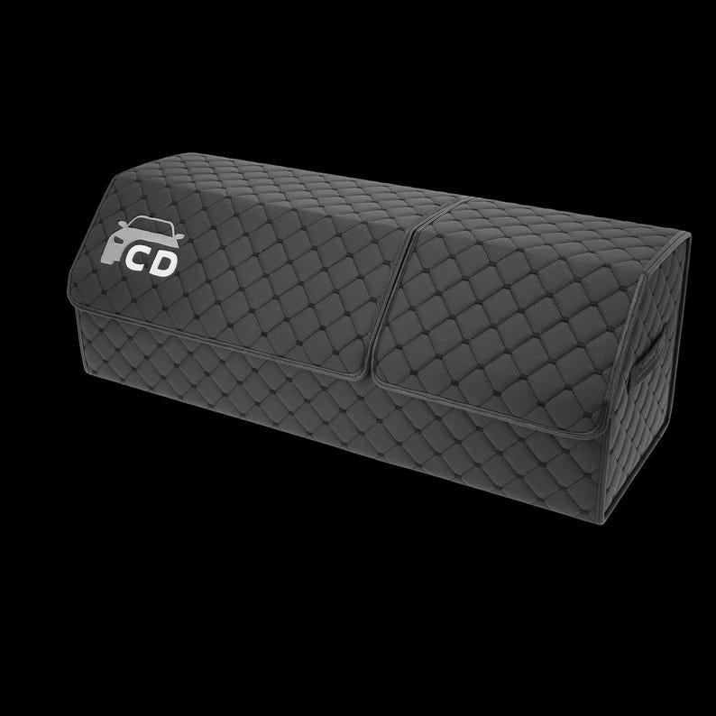 May include: A black, quilted car trunk organizer with a rectangular shape. The organizer features a diamond pattern and a white car logo with the letters "CD". It has a hinged lid and a handle on the side.
