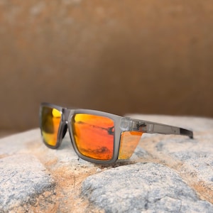 May include: Sunglasses with a matte gray frame and reflective orange lenses. The rectangular frames feature side shields and a logo on the temple. The lenses have a vibrant orange tint that reflects the surroundings, and the frame has a sturdy build.
