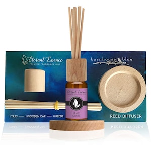 May include: A reed diffuser set featuring a small amber glass bottle with a wooden cap and eight reeds. The label reads Eternal Essence Premium Fragrance Oils Lilac & Lilies. Includes a circular wooden tray and an extra wooden cap on a blue card.