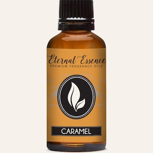 May include: An amber glass bottle with a black cap containing fragrance oil. The label features the text Eternal Essence Premium Fragrance Oils and Caramel, with a central circular logo displaying a white leaf graphic on a black background.