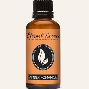 Puede incluir: Un frasco de vidrio ámbar con tapa de rosca negra que contiene aceite aromático. La etiqueta es naranja con texto negro que dice Eternal Essence Premium Fragrance Oils y Amber Romance, con un logotipo circular y un gráfico de hoja blanca.