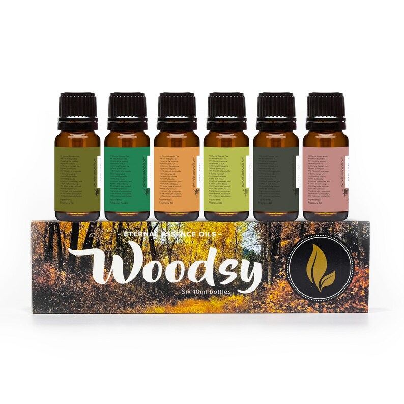 Puede incluir: Seis frascos de vidrio &aacute;mbar con tapas negras, cada uno con 10 ml de aceite esencial, dispuestos sobre una caja rectangular. La caja muestra una escena de bosque, el texto "Eternal Essence Oils", "Woodsy", "Six 10ml bottles" y un logo.