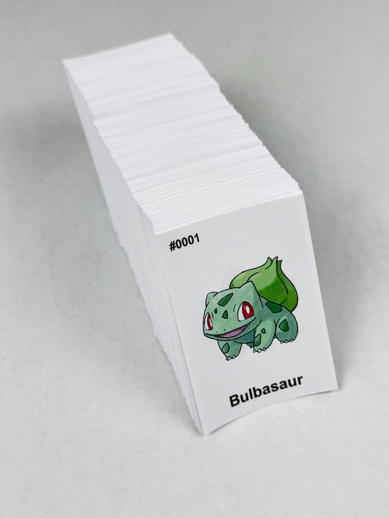 May include: A stack of rectangular white cards featuring a printed illustration of a green Bulbasaur character with a bulb on its back. The text #0001 is printed in black above the character, and the name Bulbasaur is printed in black below it.