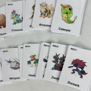 May include: A collection of white rectangular trading cards featuring colorful illustrations of various creatures. Each card displays a unique character, a corresponding identification number, and a name printed in black text at the bottom.