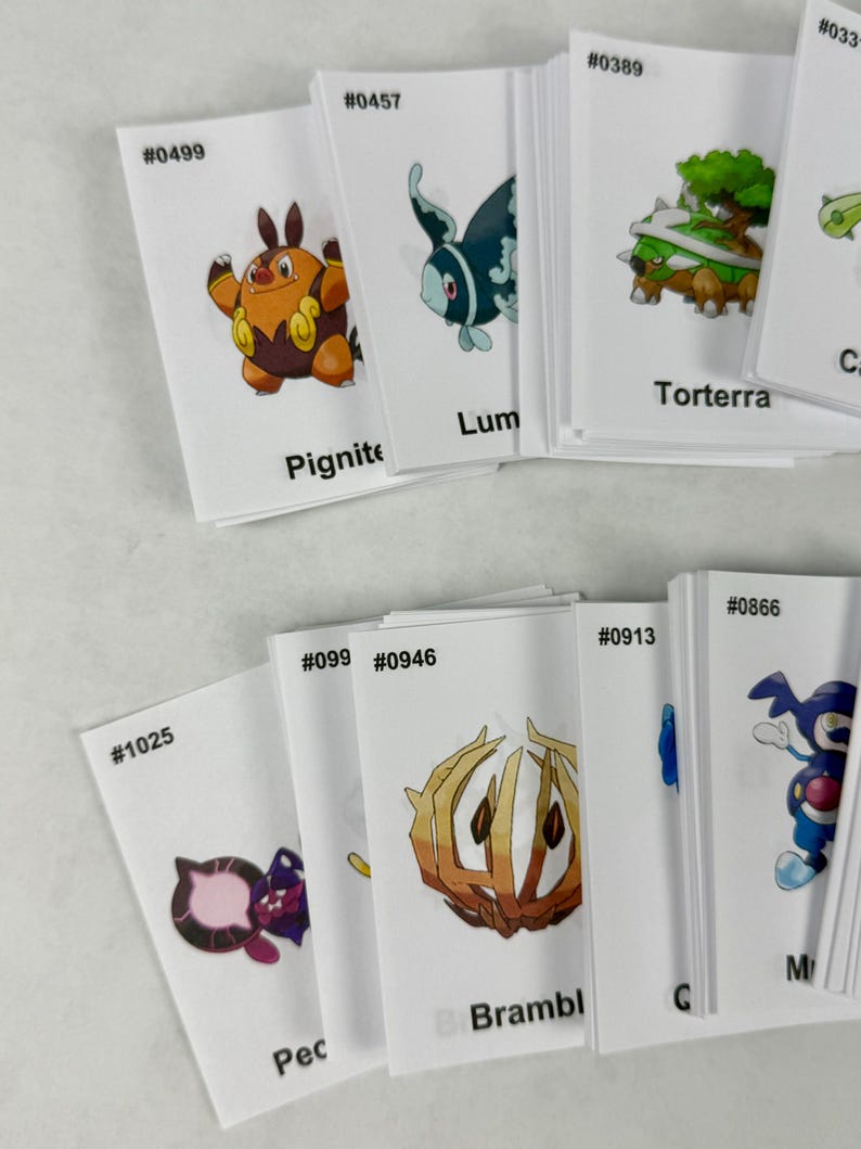 May include: A collection of white rectangular cards featuring colorful illustrations of various creatures. Each card displays a unique identification number, such as #0499, #0457, #0389, #1025, #0946, #0913, and #0866, along with names like Pignite, Torterra, and Bramblin.