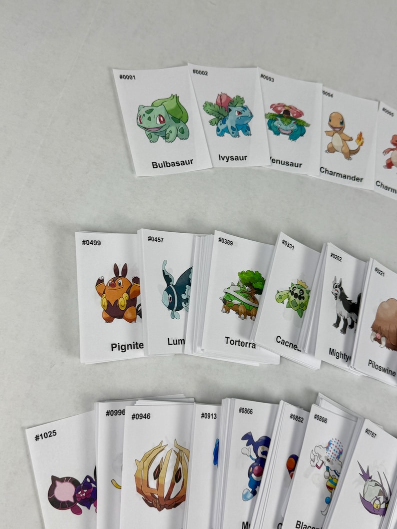May include: A collection of white rectangular trading cards featuring colorful illustrations of various creatures. Each card displays a unique identification number, a character name, and a specific creature graphic, arranged in rows on a plain surface.