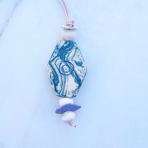 May include: A blue and white marbled hexagon pendant with white and purple beads on a pink cord.