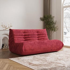 May include: A red corduroy sofa with a low profile and rounded edges. The sofa has a three-cushion back and a wide, comfortable seat. The fabric has a textured appearance. The sofa is a modern piece of furniture.