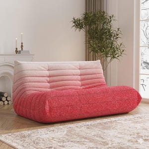 May include: A modern, low-profile sofa in a gradient of pink hues. The plush, textured fabric transitions from a light pink at the top to a vibrant red at the base. The sofa features a unique, segmented design, perfect for a contemporary living space.