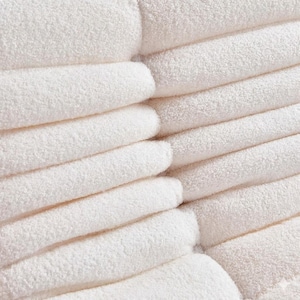 May include: Close-up of a stack of folded, fluffy white towels. The towels are neatly arranged, showcasing their soft texture and clean appearance. The image highlights the absorbent material, perfect for bathroom or spa use.