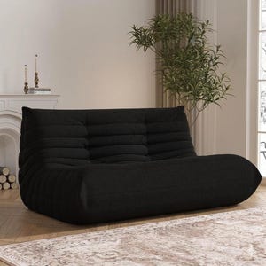 May include: A black, low-profile sofa with a rounded shape and a textured, ribbed design. The sofa is positioned in a room with a neutral color palette, a fireplace, and a large window.