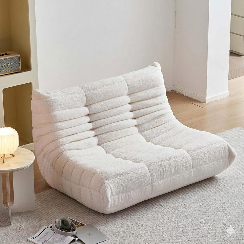 May include: A white, low-profile, modular sofa with a textured, ribbed design. The sofa is made of a soft, plush material and is designed for comfortable seating. The modern, minimalist design is suitable for a living room or lounge area.