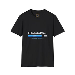 May include: Black t-shirt with the text "STILL LOADING..." above a blue progress bar labeled "FAITH" and the text "PLEASE BE PATIENT" below. The shirt has a crew neck and short sleeves.