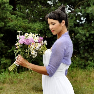 Lilac mohair wedding shrug with 3/4 long sleeves. Bride is standing on a field, wearing lilac colour bolero and white dress.