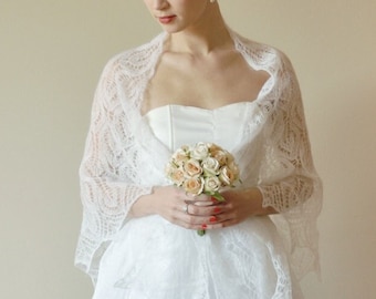 May include: A bride wearing a white strapless gown with a delicate lace shawl and holding a bouquet of light peach roses.