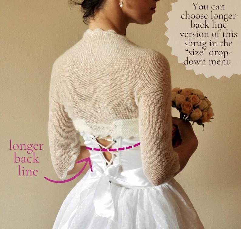 May include: A cream-colored knit shrug with three-quarter length sleeves worn over a white satin dress featuring a lace-up back closure with a ribbon tie. Text on the image reads: You can choose longer back line version of this shrug in the size drop-down menu and longer back line.