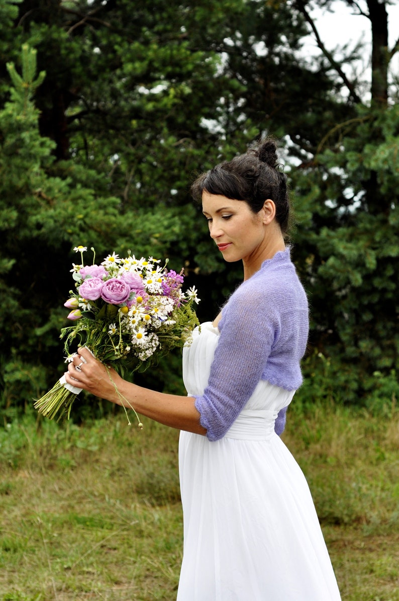 Lilac mohair wedding shrug with 3/4 long sleeves. Bride is standing on a field, wearing lilac colour bolero and white dress.