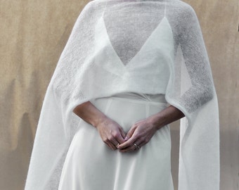 May include: A white knitted shawl with a delicate open weave, draped over a white dress. The shawl has a simple, elegant design and is perfect for adding a touch of warmth and style to any outfit.