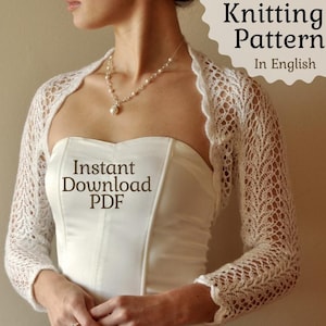 May include: A white, lacy knitted bolero with long sleeves. The bolero is worn over a white strapless top. The image includes the text "Knitting Pattern In English" and "Instant Download PDF". A pearl necklace is also visible.