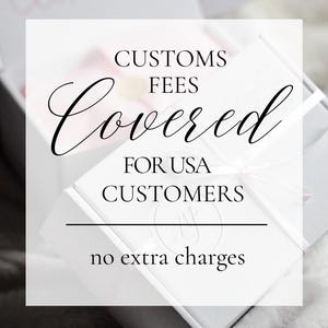 May include: A white square box with a light pink ribbon, featuring black text that reads: CUSTOMS FEES Covered FOR USA CUSTOMERS, with a horizontal line and the text no extra charges below it, presented on a soft, light-colored surface.