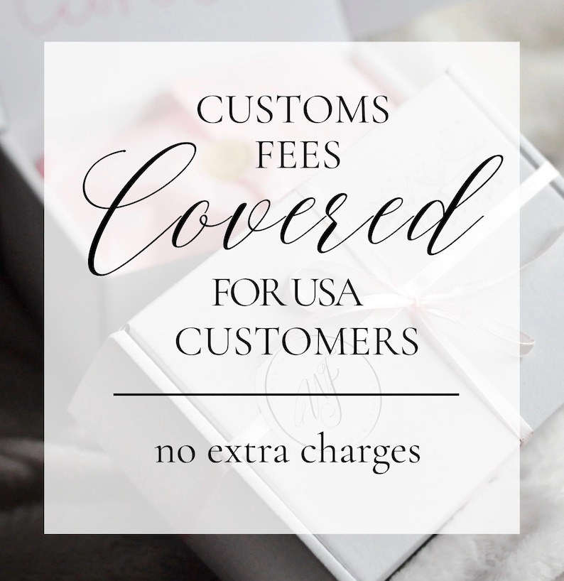 May include: A white square box with a light pink ribbon, featuring black text that reads: CUSTOMS FEES Covered FOR USA CUSTOMERS, with a horizontal line and the text no extra charges below it, presented on a soft, light-colored surface.