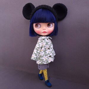 May include: A doll with black ears, a black and white hat, a green and white floral jacket, and blue shoes. The doll has blue eyes and black hair.