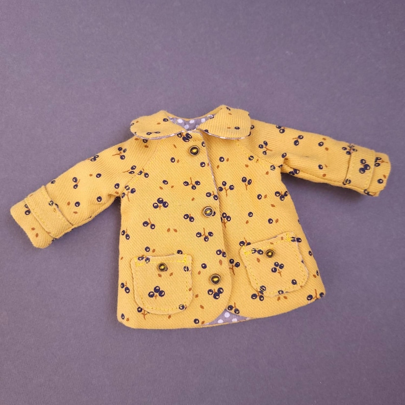 May include: A yellow jacket with a black and white floral print and two pockets. The jacket has a white collar and buttons.