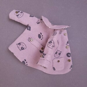 May include: A pink baby jacket with a panda print and gold buttons. The jacket has a small pocket on the front.