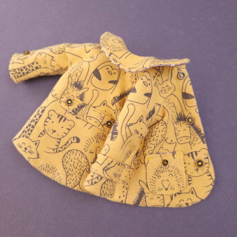 May include: A yellow children's coat with a black and white animal print. The coat has a peter pan collar and a button closure.