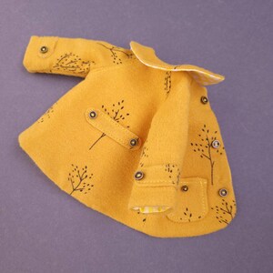 May include: A yellow coat with a white collar and black tree designs. The coat has multiple buttons and pockets.