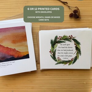 May include: A set of printed cards with envelopes featuring two designs: one with a watercolour sunrise landscape and the text "the dawn from on high will break upon us," and another with a pine wreath and the text "He took upon His head the thorns that sin had produced, that He might crown our souls with grace."