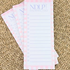 Peut inclure: Plusieurs blocs-notes de listes de courses à carreaux roses et blancs. Chaque bloc-notes porte l'inscription "NDLP SHOPPING LIST" en lavande. Les blocs-notes ont un format de liste de contrôle avec des lignes vierges.