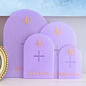 May include: Four lavender arch-shaped display boards with a textured chevron pattern. Each board features a gold cursive logo and a central cross-shaped cutout. The sizes printed on the boards are 9.0, 6.0 x 4.0 in, and 4.5 x 3.0 in.