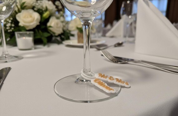 Close-up of personalized wedding wine glass charms used as guest names and drink markers.