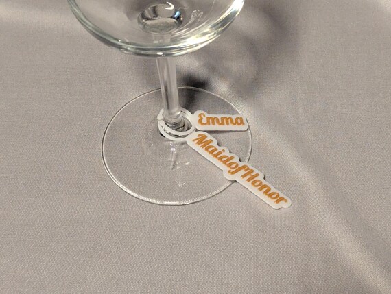 Personalized Emma maid of honor wine glass charm shown close up on a decorated reception table.