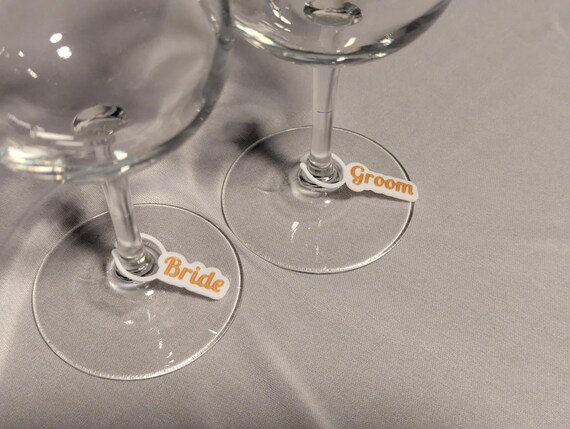 Close-up side view of bride and groom name charms resting around two wine glass stems.