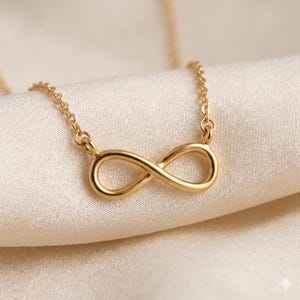 Peut inclure: Un collier doré avec un pendentif en forme de symbole infini. Le pendentif, une boucle continue, est suspendu à une chaîne délicate. Le collier est présenté sur un tissu crème, soulignant sa finition polie.