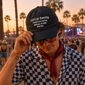 May include: A black baseball cap featuring white embroidered text that reads Let's go dancing, I want to go dancing with you all night dancing. The cap has a structured crown and a curved brim, designed with a classic six-panel construction.
