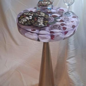 Mesa de apoio em resina, rosas roxas, pedrinhas brancas, pedestal cônico preto.
