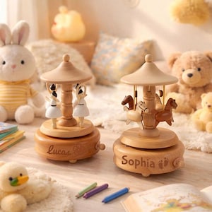 Könnte beinhalten: Zwei hölzerne Karussell-Spieluhren. Eine zeigt Ballerina-Figuren, die andere Pferdfiguren. Beide sind hellbraun mit einem gewölbten Dach und einem kreisförmigen Sockel. Auf der Basis steht "Lucas", auf der anderen "Sophia".