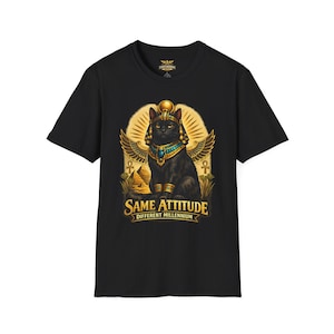 May include: Black t-shirt featuring a graphic of an Egyptian cat with a golden headdress, wings, and jewelry. The text "SAME ATTITUDE DIFFERENT MILLENNIUM" is below the cat. The design includes pyramids and hieroglyphs.