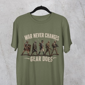 Könnte beinhalten: Olivgrünes T-Shirt mit einer Grafik von Soldaten aus verschiedenen Epochen, die in einer Reihe marschieren. Der Text "WAR NEVER CHANGES GEAR DOES" ist oberhalb und unterhalb der Soldaten in weißer Schrift gedruckt.