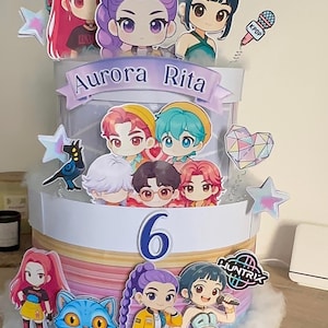 May include: A multi-tiered cake decorated with cartoon figures, stars, and the number 6. The cake features the text "Aurora Rita" and "Huntrix". The cake is decorated with a variety of colourful elements.