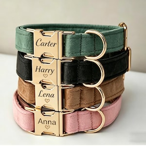 May include: A stack of four personalized dog collars in various colors: green, black, brown, and pink. Each collar features a gold-colored buckle engraved with a name and a heart symbol. The collars are stacked on top of each other.
