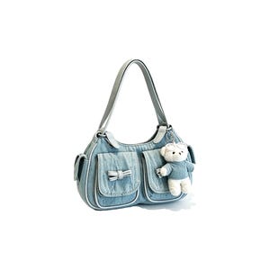 Puede incluir: Bolso de hombro de mezclilla azul claro con dos bolsillos delanteros y un peque&ntilde;o detalle de lazo. El bolso tiene un ribete blanco y un asa a juego. Un peque&ntilde;o llavero de oso de peluche cuelga del lateral.