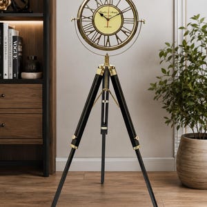 May include: A floor clock featuring a circular brass frame with Roman numerals and a cream-colored face labeled Franklin & Murphy Est 1888 Oxford. The clock is mounted on a black wooden tripod stand with brass accents and adjustable legs.