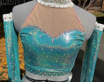 May include: A teal, sequined dance costume displayed on a mannequin. The costume includes a crop top, skirt, arm sleeves, and a headpiece. The top features a sweetheart neckline and a sheer mesh panel. The costume is embellished with iridescent rhinestones and has the word "WAIST" on the waist band.