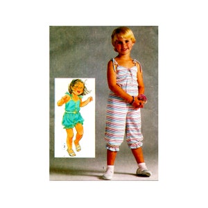 May include: A young girl wearing a striped, white, pink, and blue jumpsuit with a ruffled hem. The jumpsuit has thin straps and a button closure. The girl is holding a small bouquet of pink flowers.