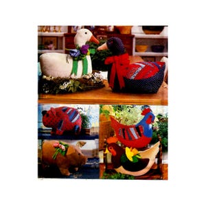 May include: A collection of fabric stuffed animal figures including a white goose with a green ribbon, a dark blue patterned goose with a red bow, two pigs with red and brown fabric, and two chickens featuring red, blue, and brown fabric accents.