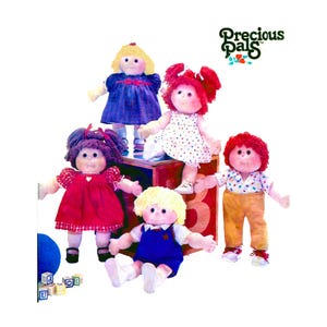May include: A collection of six Precious Pals dolls. The dolls have soft, round faces and yarn hair in various colors. They are dressed in colorful outfits, including dresses, overalls, and shirts. The dolls are posed on a red and brown block.